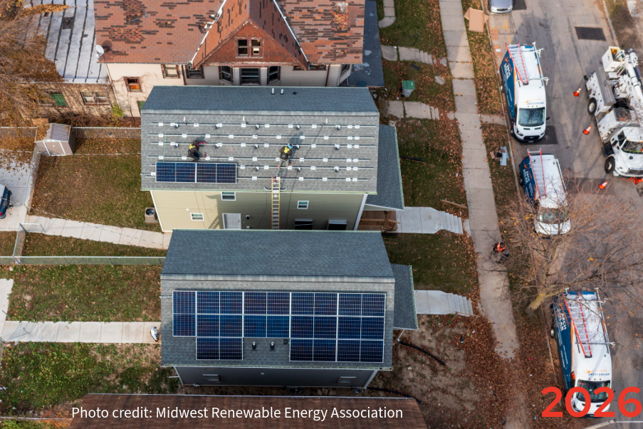 Aerial view of residential rooftops, one of which has solar panels and another of which is in the process of having solar panels installed.